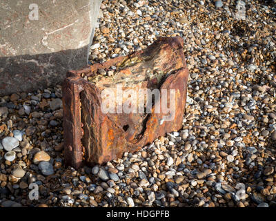 I resti arrugginiti di mare di strutture di difesa su una spiaggia ghiaiosa Foto Stock