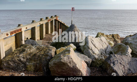 Pennelli in legno in esecuzione da una spiaggia di ciottoli in mare con la linea di orizzonte e rocce in primo piano Foto Stock