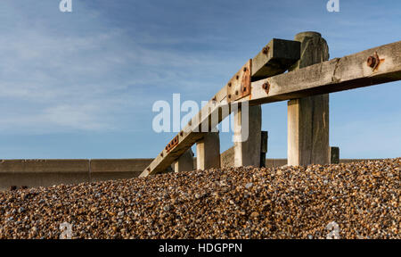 Pennelli in legno in esecuzione da una spiaggia di ciottoli di un mare muro contro un cielo blu Foto Stock