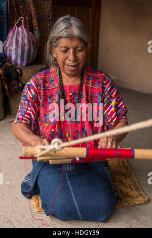 Un vecchio, grigio-dai capelli donna Maya tesse tessuto su un telaio dorsalino mentre inginocchiati sul pavimento della sua casa di Santa Catarina Palopo, Guatemala. Foto Stock