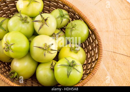 Pomodori verdi in un cesto di vimini su un tavolo di legno Foto Stock