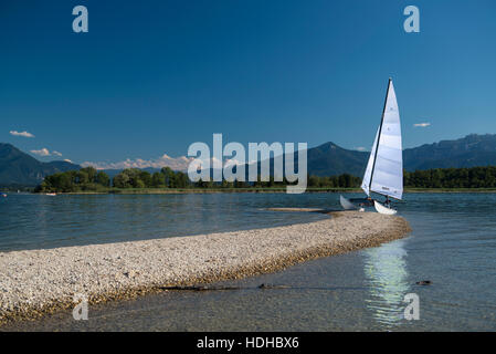 Outrigger barca a vela ormeggiata su lakeshore contro il cielo blu, il Lago Chiemsee, Baviera, Germania Foto Stock