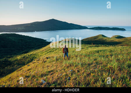 Vista posteriore di un escursionista in piedi sul campo erboso mentre guardando il mare orientale contro sky Foto Stock