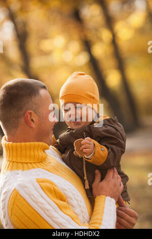 Allegro baby boy essendo portati dal padre al parco durante l'autunno Foto Stock