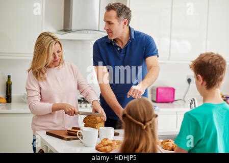 Una famiglia di quattro persone, genitori e due bambini prepara la colazione in cucina. Foto Stock