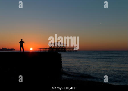 Stagliano uomo in piedi su groyne guardando sunrise tra banchine di Brighton Foto Stock