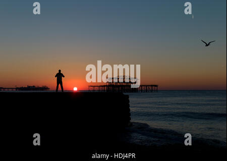 Stagliano uomo in piedi su groyne guardando sunrise tra banchine di Brighton Foto Stock