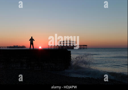 Stagliano uomo in piedi su groyne guardando sunrise tra banchine di Brighton Foto Stock