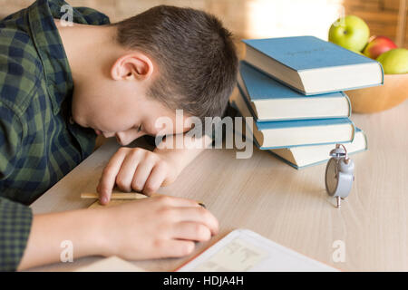 Stanco Schoolboy addormentato su una scrivania mentre si fanno i compiti a casa Foto Stock