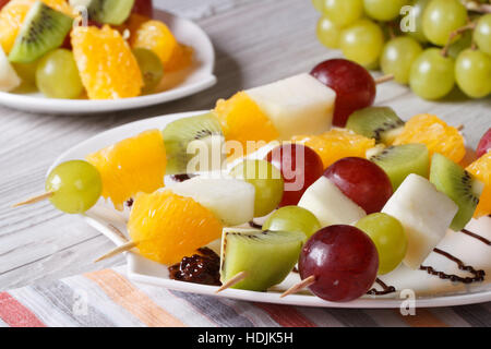 Un dessert di frutta fresca su spiedini su una piastra bianca di close-up orizzontale. Foto Stock