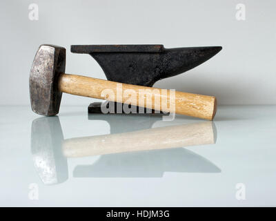 Ancora una vita con gli strumenti del fabbro, un martello e una vecchia incudine su una lastra di vetro con sfondo bianco. Foto Stock