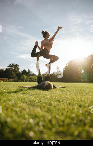 Colpo verticale di una sana coppia giovane facendo yoga acrobatico sull'erba. L uomo e la donna che esercitano in coppia al parco. Foto Stock