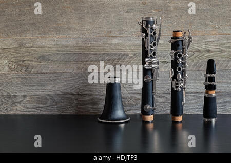 Black clarinetto smontabile in quattro parti su una tavola nera con un alterato grigio Sfondo di legno Foto Stock