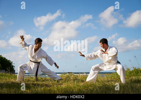 Lotta e sport estremi. Gli uomini di origine ispanica che esercitano nel karate tradizionale e arti marziali. Simulazione di lotta sulla spiaggia vicino al mare Foto Stock