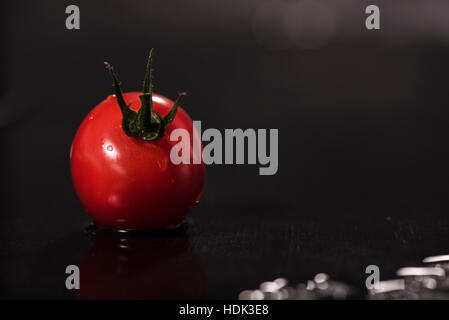 Uno mature, pomodori rossi con gocce di acqua sul tavolo, su sfondo scuro Foto Stock