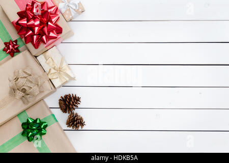 Molti regali di Natale scatole allineate come bordo sinistro con coppia pigne su bianco colorate tavole di legno con copia spazio sul lato destro del f Foto Stock