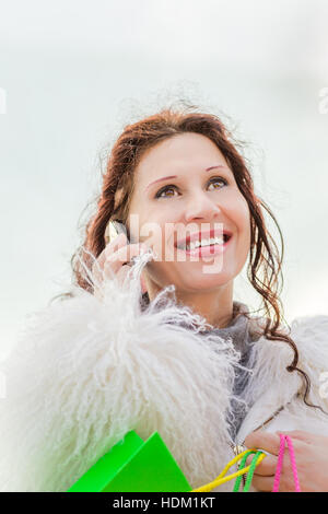 Donna felice menopausal che parla al telefono mentre tiene i sacchetti colorati dello shopping Foto Stock