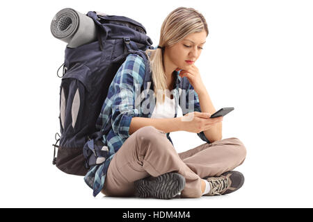 Escursionista femmina seduto per terra e guardando un telefono cellulare isolato su sfondo bianco Foto Stock