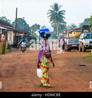 Donna in strada di Kenema, in Sierra Leone, che porta un grande cesto sulla sua testa Foto Stock