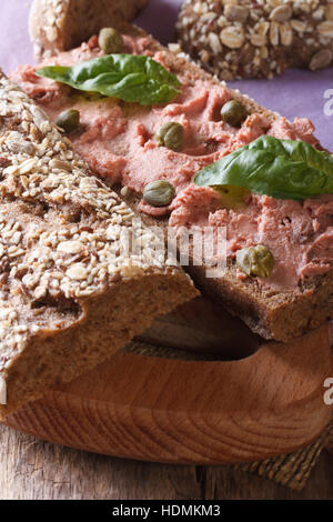 Sandwich con pate, capperi e basilico close-up sul tagliere. In verticale Foto Stock