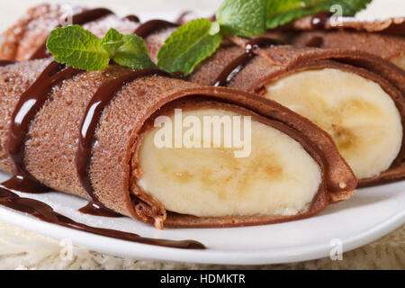 Crepes di cioccolato con ripieno di banana macro su una piastra bianca orizzontale. Foto Stock