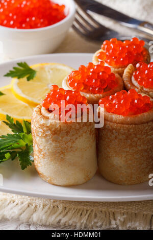 Pancake bobine con caviale rosso su una piastra e limone. In verticale Foto Stock