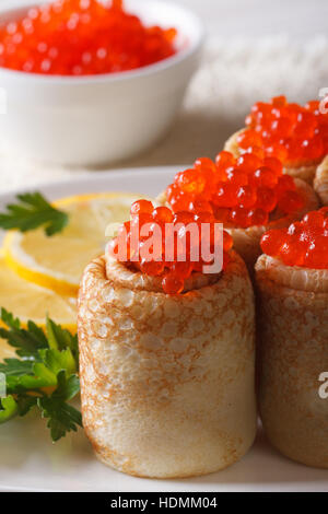 Rotoli per pancake riempito con caviale rosso su una piastra macro verticale. Foto Stock