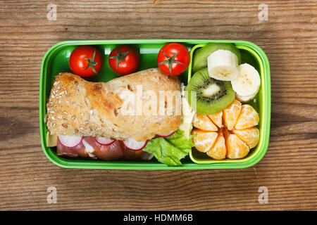 Lunchbox sul tavolo di legno. Panino di prosciutto e frutta in scatola di plastica Foto Stock