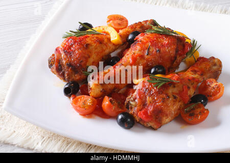 Stufati di cosce di pollo in salsa di pomodoro con peperoni e olive e rosmarino su una piastra bianca, orizzontale Foto Stock