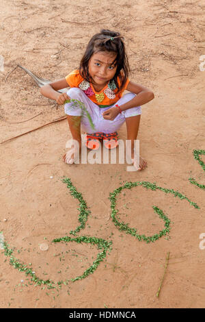 A cinque anni ragazza cambogiano apprende il suo alfabeto Khmer utilizzando frammenti di foglie disposti nella sporcizia in Cambogia. Foto Stock