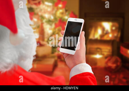 Santa Claus tenere white smart phone con schermo vuoto per mockup. Il tempo di Natale con camino in background. Foto Stock