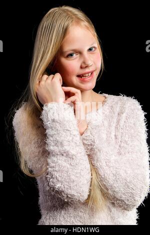 Capelli biondi ragazza in luce maglione rosa su sfondo nero Foto Stock