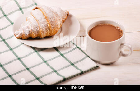 Una deliziosa tazza di caffè e un croissant su una tovaglia e sfondo di legno Foto Stock