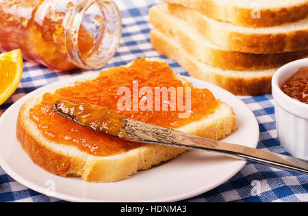 Fette di pane con marmellata di arancio per la colazione sulla tovaglia a scacchi Foto Stock