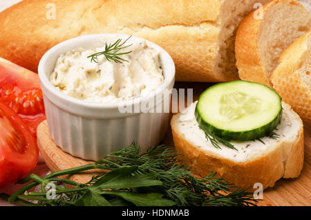 Baguette croccanti fette con la crema di formaggio con erbe e verdure sul tagliere per la prima colazione Foto Stock