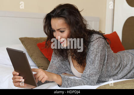 Donna controllo tablet a casa sdraiato sul letto Foto Stock