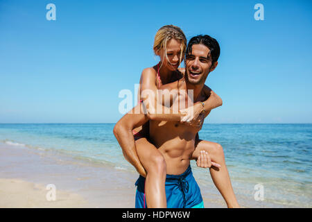 Ritratto di uomo che porta ragazza sul suo retro. Giovane godendo piggyback ride sulla spiaggia vacanza. Foto Stock