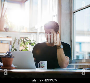 Giovane uomo d affari con stress guardando al suo computer portatile in ufficio. Executive maschio concentrare sul lavoro. Foto Stock