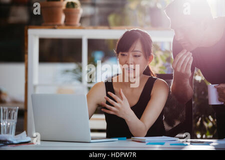 Colpo di due giovani colleghi di lavoro guardando il laptop. Gli imprenditori che lavorano insieme sul computer portatile in ufficio. Foto Stock