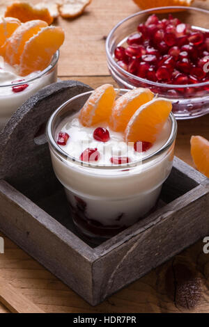 Lo yogurt con i semi di melograno e mandarino sul tavolo di legno Foto Stock