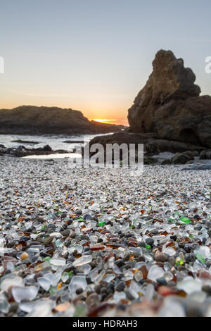 Arancione tramonto sulle rocce dando una luce morbida per i colori del mare di vetro in questa spiaggia Foto Stock