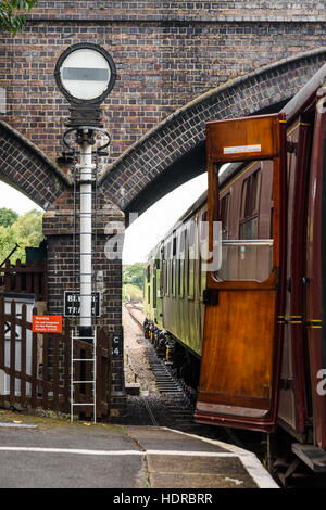 In treno la piattaforma con la porta aperta a Toddington stazione ferroviaria accanto a un ponte e banner segnale ripetitore Foto Stock