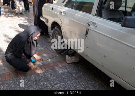 Una donna usa un martinetto tand un mattone per riparare la vettura danneggiata in Shiraz, Far, Provincia, Iran. Foto Stock