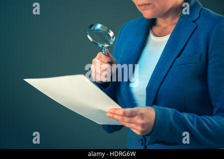 Femmina ispettore fiscale guardando corporate documenti finanziari con lente di ingrandimento Foto Stock