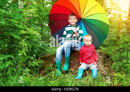 Bambini seduti nel parco con ombrello coloratissimo Foto Stock