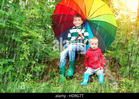 Bambini seduti nel parco con ombrello coloratissimo Foto Stock