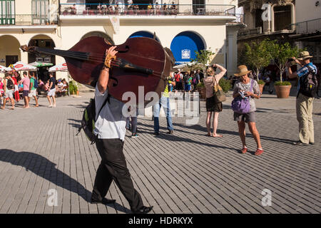 Musicista portando la sua double bass sulla sua spalla attraverso la Plaza Vieja, La Habana Vieja, La Havana, Cuba. Foto Stock