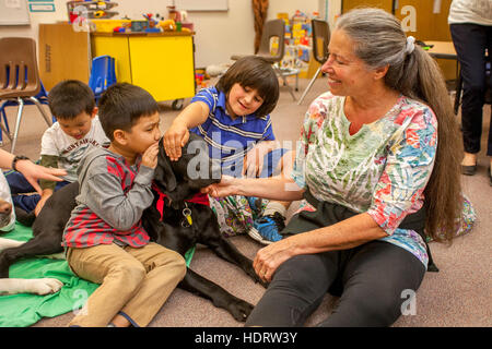 Multirazziale giovani studenti abbraccio una terapia cane sul pavimento di una scuola elementare in classe Mission Viejo, CA. Nota insegnante. Foto Stock