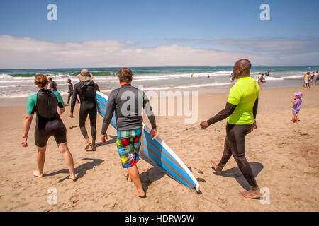 Grazie per il suo servizio militare, un veterano (destra) riceve gratuitamente una lezione di surf da un istruttore femmina (sinistra) come essi a piedi l'Oceano Pacifico in Huntington Beach, CA. Foto Stock