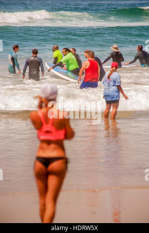 Grazie per il suo servizio militare, un veterano riceve gratuitamente una lezione di surf da un istruttore femmina (sinistra) come essi wade nell'Oceano Pacifico in Huntington Beach, CA, come scarsamente placcati donna orologi. Foto Stock
